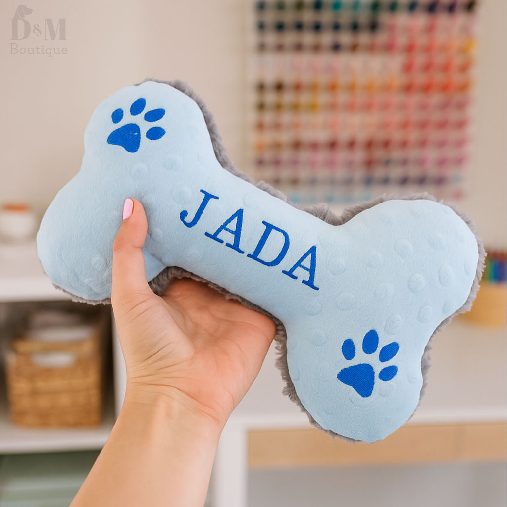 Bone-shaped pet toy with 'JADA' branding held by a hand, against a blurred indoor background.