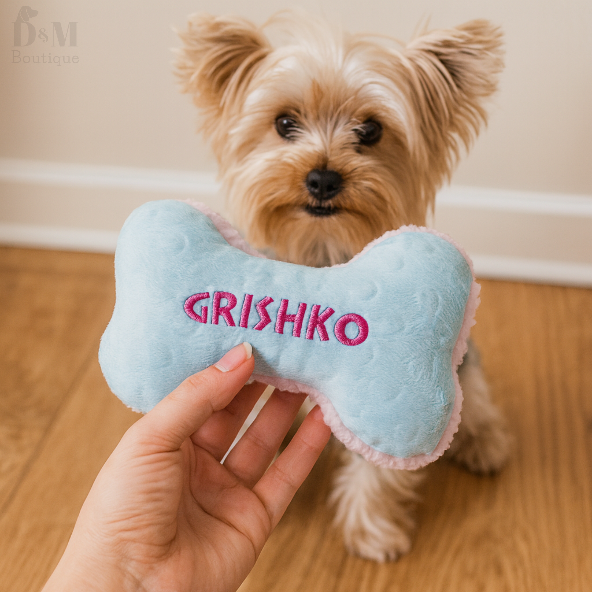 Dog holding a blue bone-shaped toy with 'GRISHKO' embroidered on it.