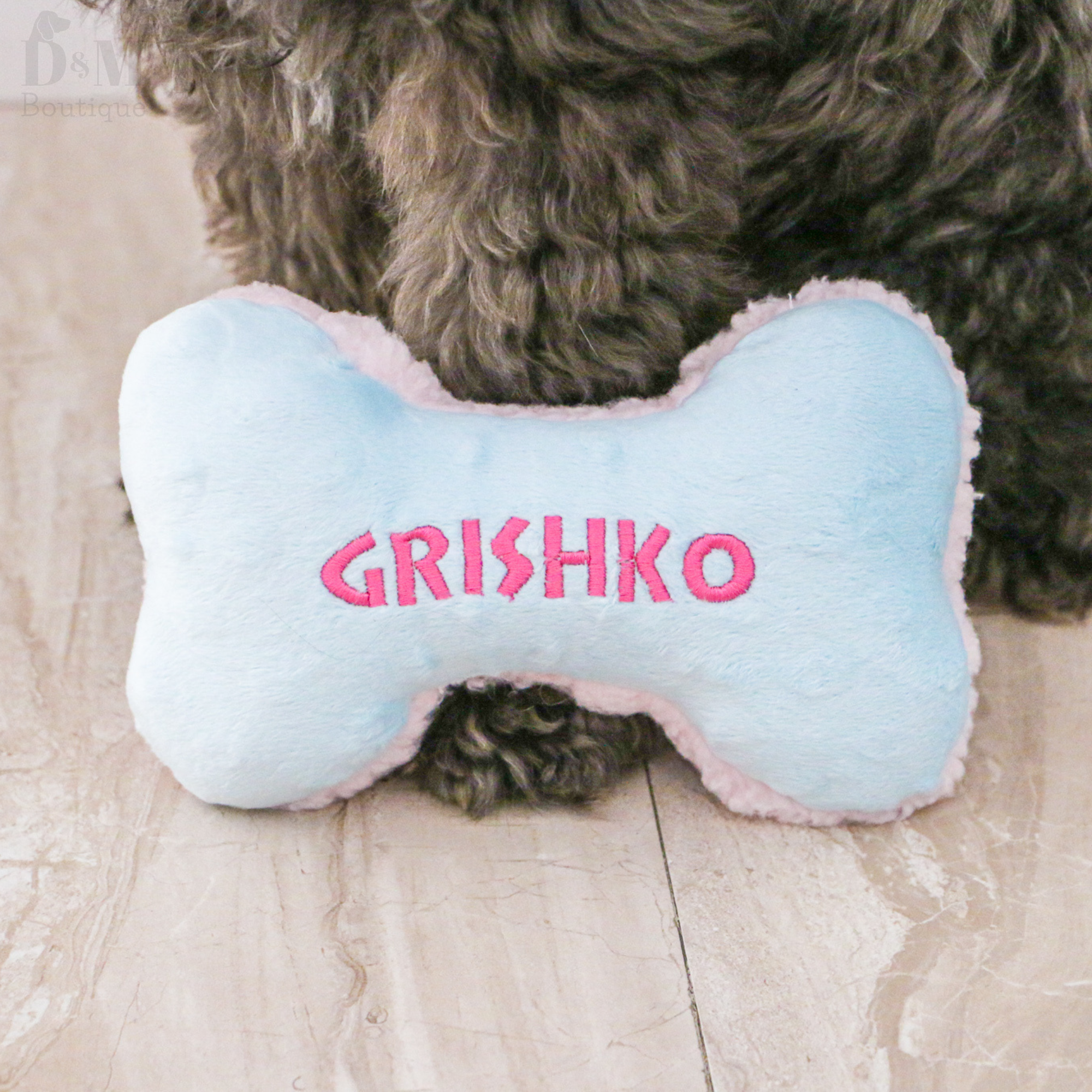 Dog bone-shaped pillow with 'GRISHKO' embroidered on it, placed on a wooden floor.