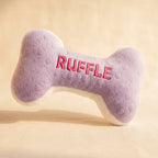 Purple bone-shaped dog toy with 'RUFFLE' embroidered on it against a light background