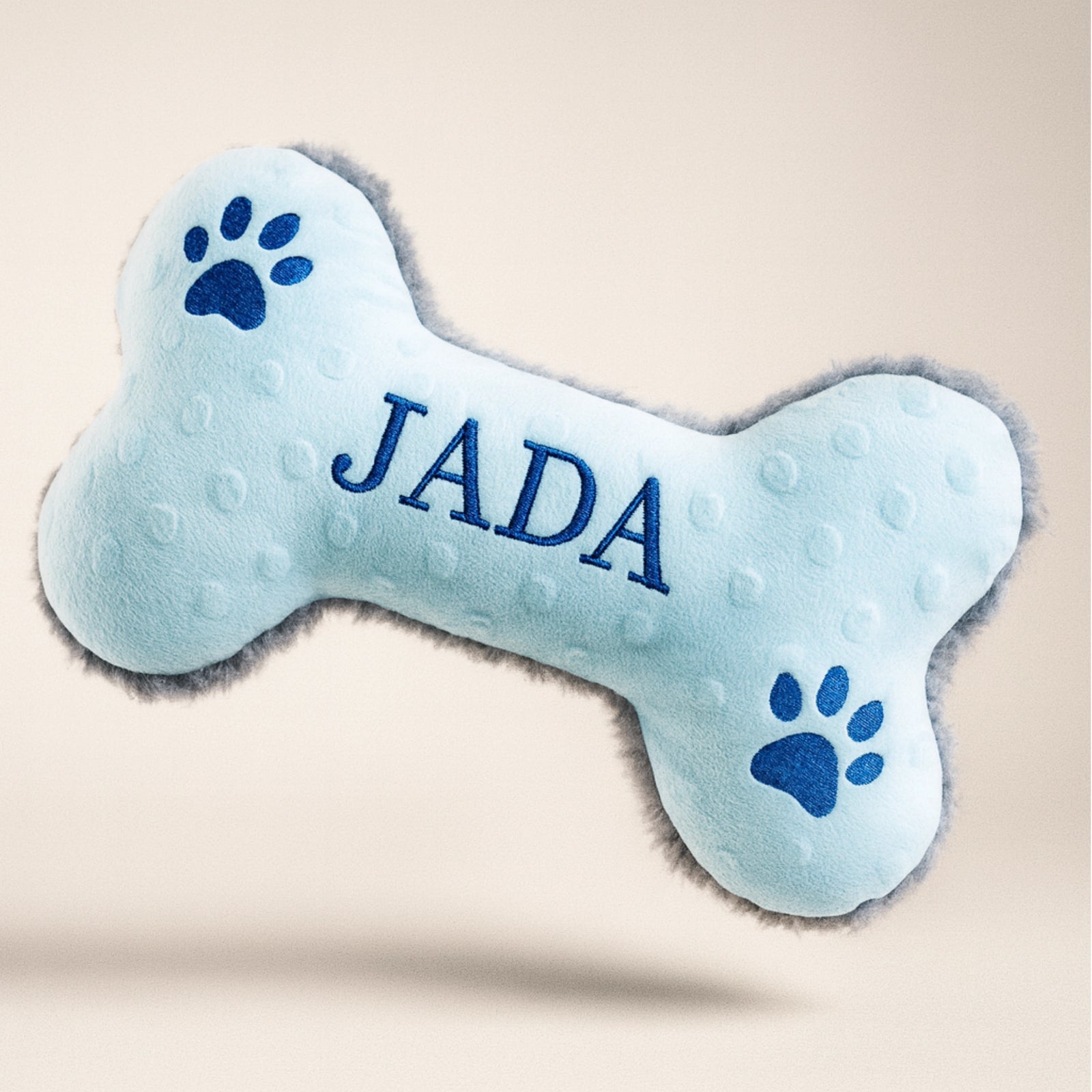 Blue bone-shaped pet toy with 'JADA' branding on a beige background