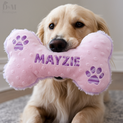 Dog holding a pink bone-shaped toy with 'MAYZIE' embroidered on it.