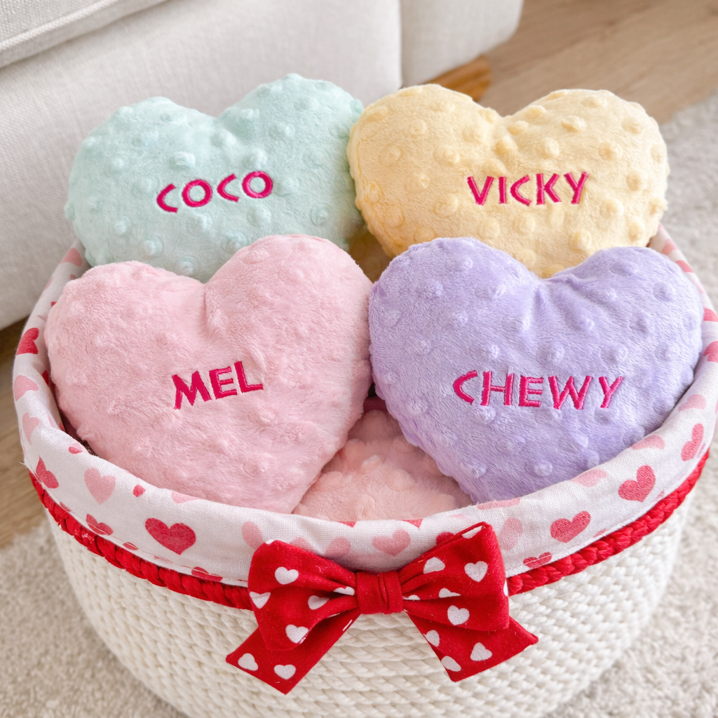 Heart-shaped plush toys with embroidered names in a basket with a red bow