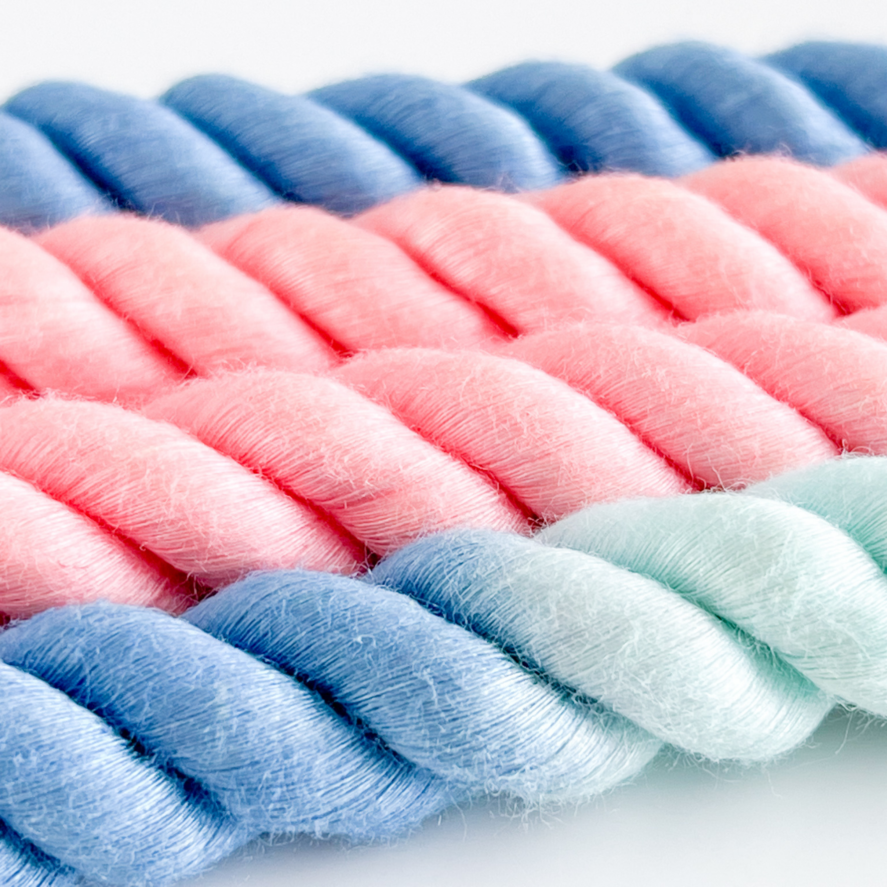 Close-up of braided yarn in pink, blue, and green on a white background